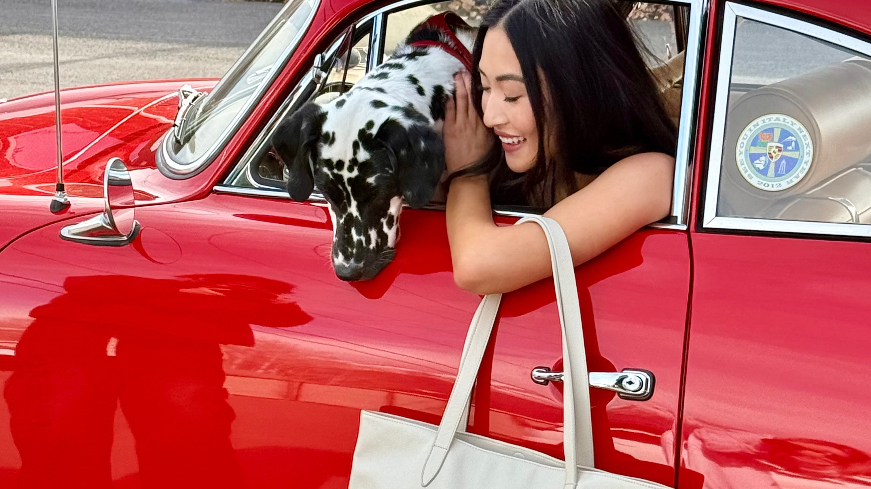 Woman with a dog in a red car, holding a white tote bag. Women with a Dalmatian. Lily Grace Cashmere Cream Tote. Luxury Leather Tote. Red Collar